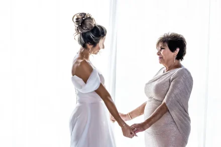 Bride holding hands with her mother during getting ready wedding moments in front of a bright window in Puerto Vallarta