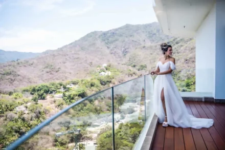 Destination wedding photography in Puerto Vallarta. A bride in a white wedding gown standing on a modern balcony overlooking tropical green hills and mountains