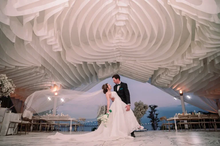A groom dipping his bride on the dance floor under an incredibly elegant draped fabric ceiling design during a wedding reception in Puerto Vallarta