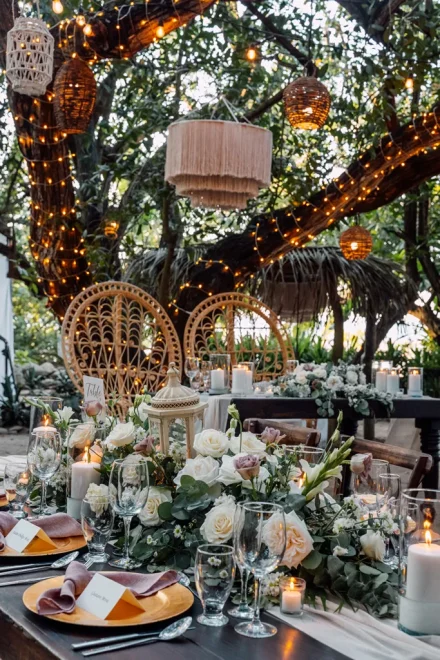 A breathtaking rustic-chic setup bathed in the warm glow of hanging lights and candles. Decorated with lush floral centerpieces and natural wicker elements, this enchanting garden table arrangement creates a cozy and romantic atmosphere for an unforgettable reception in Puerto Vallarta