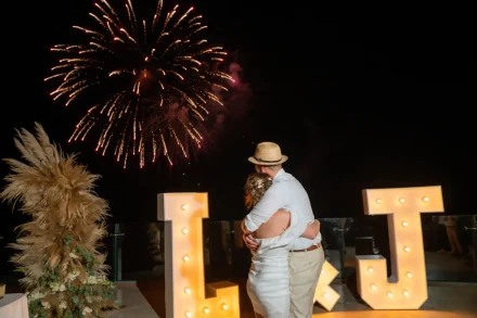 A breathtaking grand finale under a sky ablaze with fireworks. Holding each other close beside illuminated marquee initials, the newlyweds embrace the magic and wonder of an unforgettable night in Puerto Vallarta