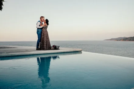Where infinity meets forever. Standing side by side above the endless horizon, their quiet kiss reflects across calm waters—capturing a dreamlike, serene moment of pure love suspended between earth and ocean in Puerto Vallarta