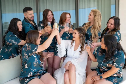 Bride in a white robe sharing a joyful toast with her bridesmaids in silk emerald pajamas during getting ready moments in Puerto Vallarta