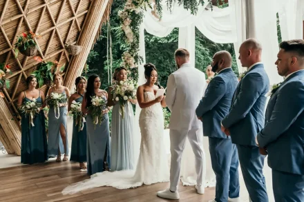 Bride holding a microphone and reading her vows to the groom during an outdoor tropical ceremony under a white canopy