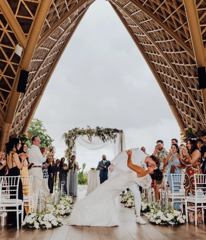 Pure, cinematic joy. After promising forever, the couple celebrates with an unforgettable kiss while their loved ones burst into applause beneath the stunning open-air chapel architecture