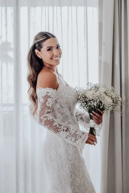 Radiant grace and pure anticipation. Standing in soft window light holding her delicate bouquet, the bride shines in timeless elegance just moments before walking down the aisle in Puerto Vallarta