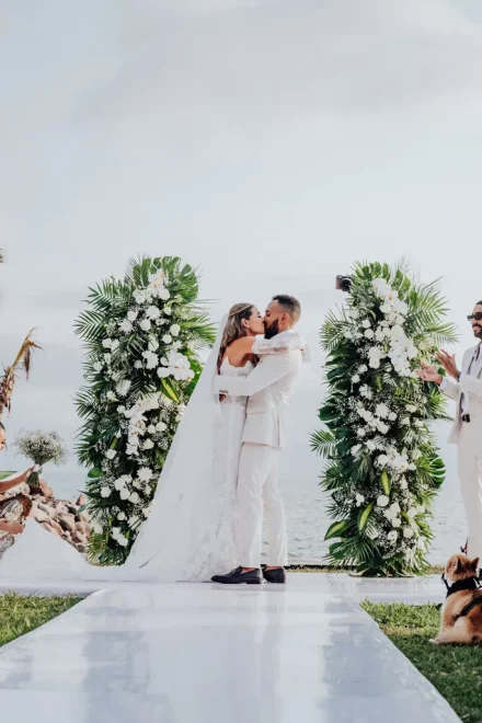 A breathtaking moment sealed with a kiss. Framed by lush tropical greenery, white orchids, and the vast ocean horizon, the newlyweds embrace as husband and wife in Puerto Vallarta