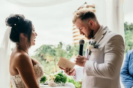Close up of the groom holding his vow booklet and speaking into a microphone while looking at his smiling bride