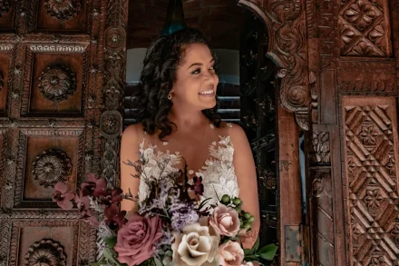 Pure joy and anticipation captured in a single, radiant glance. Framing her elegance against intricate rustic woodwork, this breathtaking bride holds her bouquet with excitement as she steps into the unforgettable beginning of her forever in Puerto Vallarta