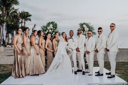 Elegance, style, and lifelong friendship against a stunning coastal backdrop. Surrounded by their beautiful bridal party in shimmering gowns and sharp white suits, the couple shares a joyous moment together on the shores of Puerto Vallarta