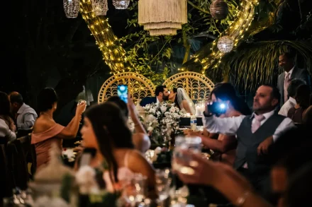 A truly candid celebration of love! Surrounded by cheering family and friends capturing the moment on their phones, the bride and groom share a passionate kiss under warm glowing lights—creating an unforgettable night in Puerto Vallarta