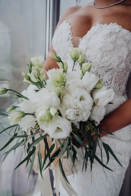 Close up shot of a bride holding a fresh white flower bouquet with eucalyptus greenery against her lace wedding dress