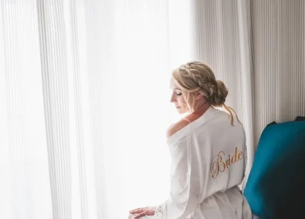 A quiet moment of reflection before the magic unfolds. Bathed in soft, natural window light, the bride wears a customized silk robe showcasing an intricate braided updo—capturing serene elegance and peaceful anticipation in Puerto Vallarta