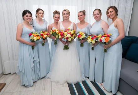 A radiant burst of color and joy. Framed by her closest friends in soft light blue gowns, the bride shines at the center holding a vibrant bouquet of tropical blooms—capturing true sisterhood and celebration in Puerto Vallarta