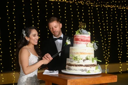A sweet tradition celebrated under a curtain of warm string lights. Hand in hand, the newlyweds slice into their beautifully decorated three-tiered cake, capturing a joyful and intimate moment during their Puerto Vallarta reception