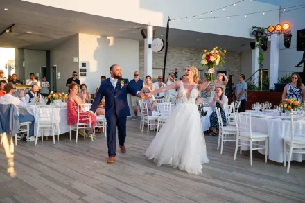 The ultimate grand entrance filled with overwhelming excitement. Cheered on by cheering friends and family, the ecstatic bride raises her colorful bouquet as she enters the open-air rooftop reception hand-in-hand with her groom in Puerto Vallarta