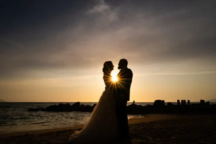 A breathtaking burst of light at dusk. Silhouetted against the glowing golden horizon, the newlyweds embrace as the setting sun flares dramatically between them—capturing pure, cinematic passion on the Puerto Vallarta coast