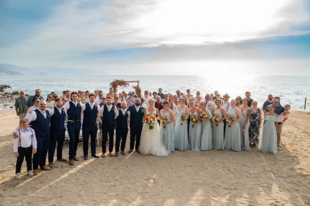 Surrounded by the warmth of family and lifelong friends. Gathered together on the shore under the soft sunlit sky, this complete group portrait captures the shared happiness and unforgettable community of a Puerto Vallarta destination wedding