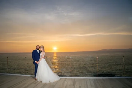 Framed by an infinite golden horizon. Standing together on a open-air rooftop terrace as the sun dips into the Pacific ocean, this stunning full-length portrait highlights pure elegance and destination romance in Puerto Vallarta