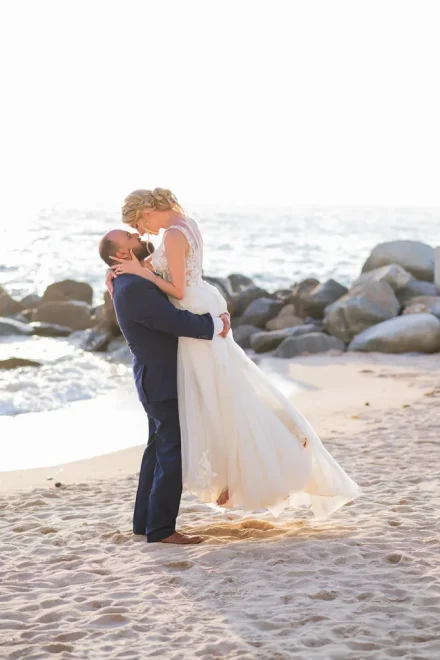 Swept up in pure bliss. Surrounded by soft golden sunlight and the gentle spray of ocean waves, the groom lifts his bride in an affectionate embrace—capturing a romantic, dreamlike moment on the shores of Puerto Vallarta