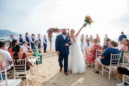 Pure, unfiltered joy as husband and wife. Cheered on by loved ones along the sandy aisle, the bride raises her vibrant bouquet in triumphant celebration—a radiant recessional moment captured on the shores of Puerto Vallarta
