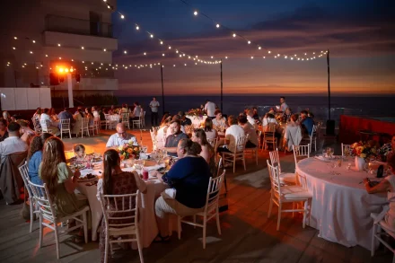 As dusk fades into night, the terrace comes alive under a canopy of glowing bistro lights. Guests dine and mingle against a dramatic twilight sky overlooking the ocean—capturing the magical, intimate atmosphere of an outdoor wedding reception in Puerto Vallarta