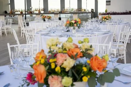 An invitation to celebrate in style. Perfectly curated with crisp white linens, fine stemware, and vibrant tropical arrangements, this reception setup sets an elegant, welcoming tone for an unforgettable evening in Puerto Vallarta