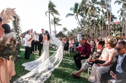 A breathtaking exchange of vows beneath towering palm trees. As the officiant speaks and loved ones look on, the sheer lace train spreads across the lawn—capturing the timeless beauty and reverent emotion of your Puerto Vallarta wedding ceremony